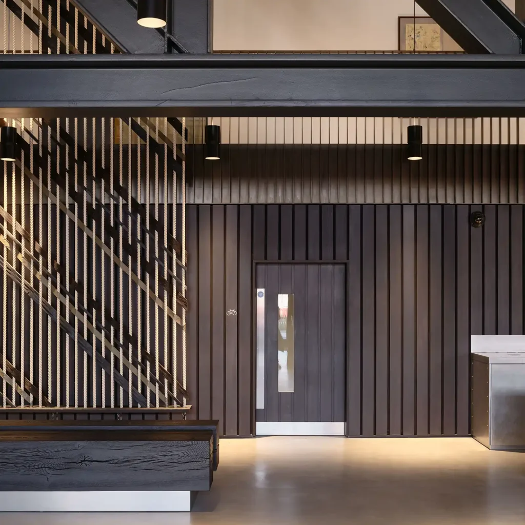 Dark timber doorset with a narrow glazed panel and stainless steel kick plate, set within matching vertical wall panelling.